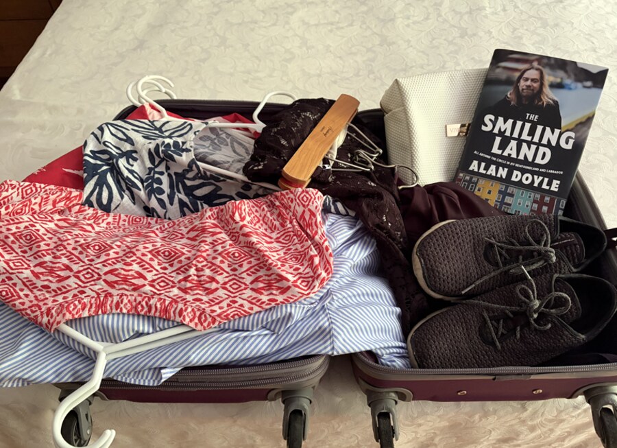 An open suitcase packed for a trip, with clothing, shoes and a book